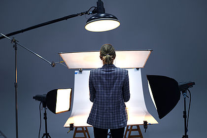 Rückansicht einer Fotografin, die vor einer Hohlkehle steht, welche von mehreren Scheinwerfern beleuchtet wird.